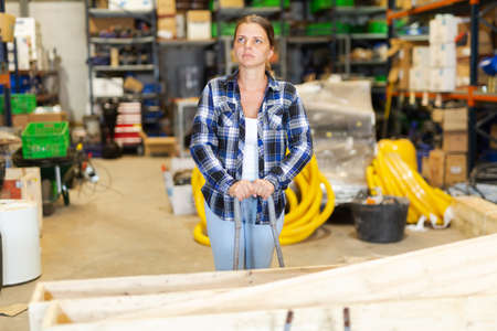 Woman carrying trolley with wooden planter boxes in large store warehouseの写真素材