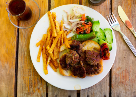 Spicy kofte (grilled minced meat) served with fresh cucumber, bread, vegetables and French fries on...