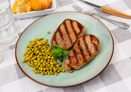 Two grilled veal steaks with canned green peas and parsley