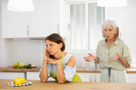 Senior woman scolding her adult daughter cooking breakfast in modern kitchenの写真素材