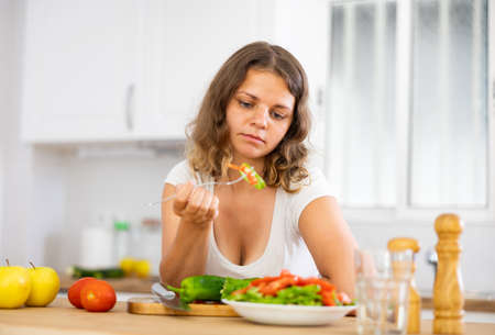 Portrait of sad woman eating salad at homeの写真素材