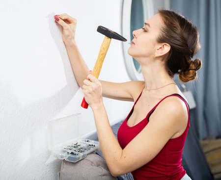 Young woman hammering a nail into the wall with hammerの写真素材