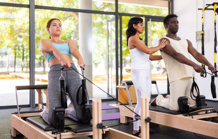 Man and woman doing exercises in pilates gym with man instructor