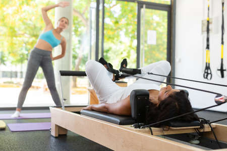 Hispanic woman pilates exercises on machines in health club.の写真素材