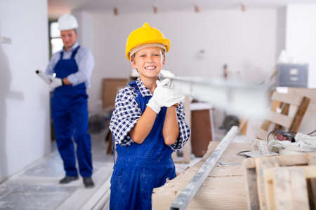 Boy in blue overalls carries an aluminum profile on his shoulder to renovate roomの写真素材