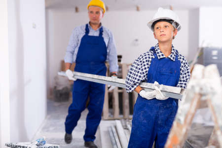 Young boy in overall carrying metal plankの写真素材
