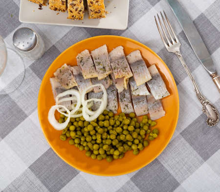 Tasty slices herring fish with canned green peas decorated by onion ringsの写真素材