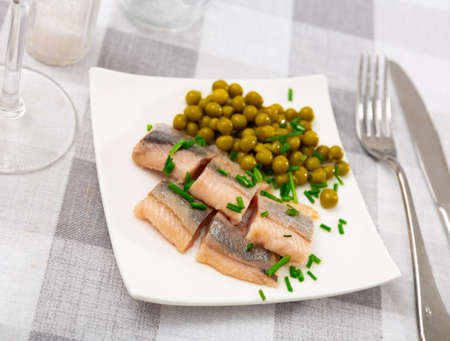 Tasty slices herring fillet with canned green peas served on plateの写真素材