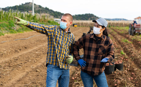 Man and woman farmers in masks standing on potato field
