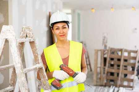 Smiling woman builder holding drill, repair works in apartmentの写真素材
