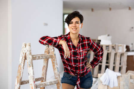 Attractive female builder standing and leaning at stepladder in apartmentの写真素材