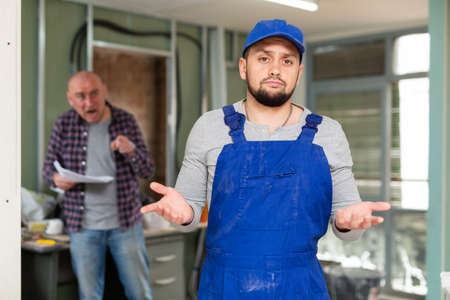 Perplexed builder in building under renovation with screaming customerの写真素材