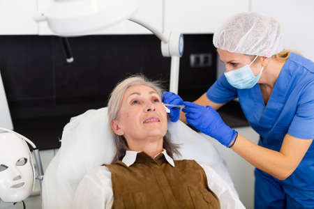 Qualified cosmetologist giving beauty injections to elderly female clientの写真素材