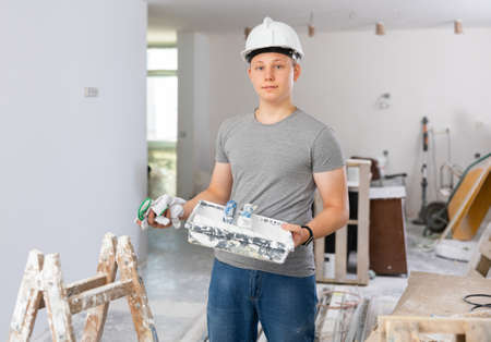 Portrait of a fifteen-year-old teenager with a roller and a paint tray in his handsの写真素材