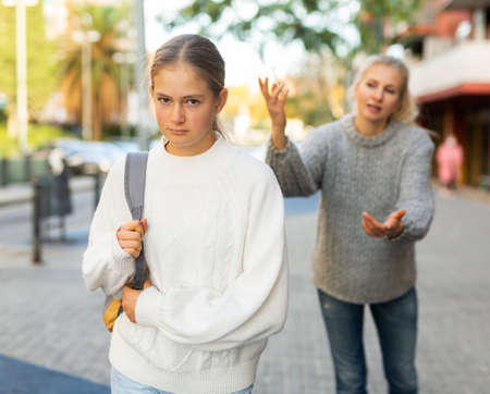 Frowning teenage girl listening to reprimanding from mother oncity streetの写真素材