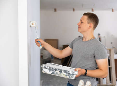 Young man painting wall with paint roller in apartment during repair worksの写真素材