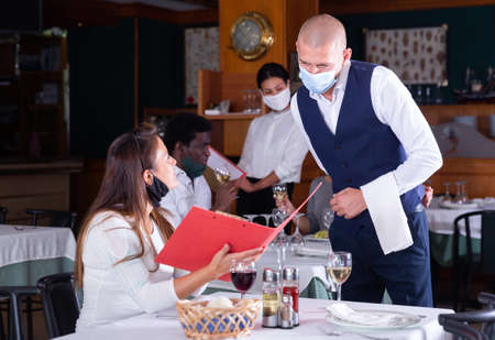 Waiter in medical mask taking order from girl in restaurantの写真素材