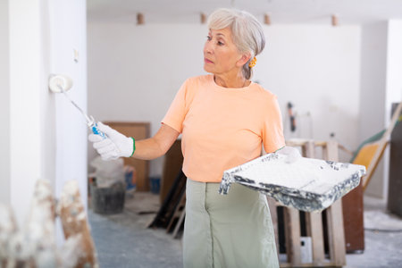 Mature woman painting walls with paint roller in refurbished roomの写真素材