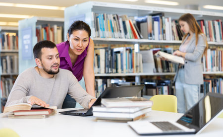 Students in the library are studying on a laptop and looking for information in booksの写真素材