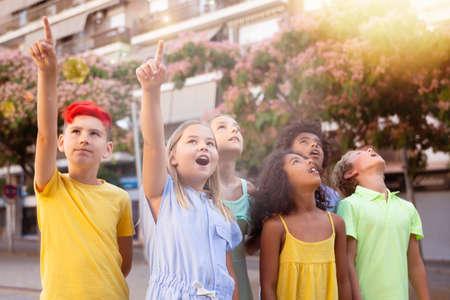 Group of surprised kids pointing fingers and looking up outdoorsの写真素材