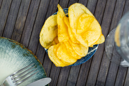 Delicious crispy potato chips in plate on table. Top view