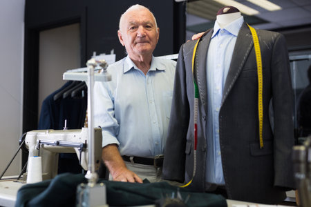 Experienced tailor tries on a new jacket on a mannequin in workshopの写真素材