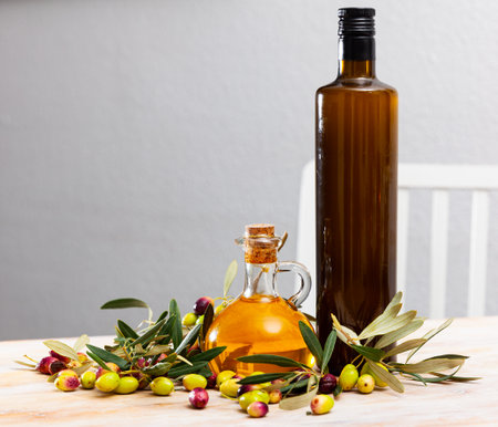 Glass bottles and carafes with fresh olive oil on wooden table with olive branches and fresh olivesの写真素材