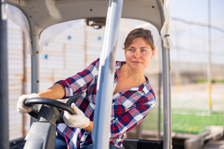 Woman gardener driving agricultural vehicle in hothouse