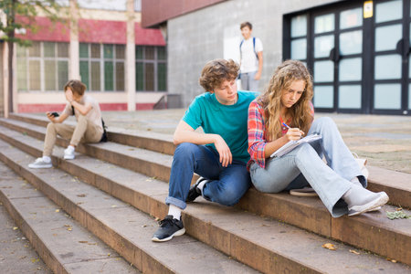 Teenage boy and girl sitting on steps near schoolの写真素材
