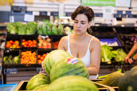 Female shopper holding watermelon in supermarket grocery sectionの写真素材