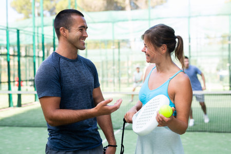 Cheerful man and woman paddle tennis players talking on open courtの写真素材
