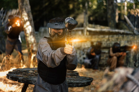 Paintball player in protective uniform aiming and shooting with gunsの写真素材