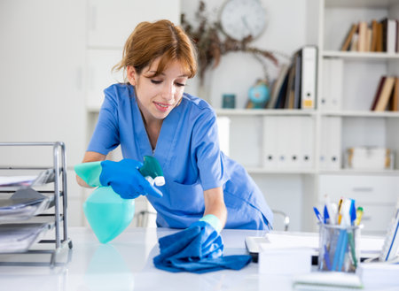 Positive woman cleaner polishing table in officeの写真素材