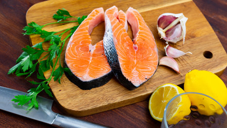 Raw salmon steaks on wooden cutting board with greens, lemon and garlicの写真素材
