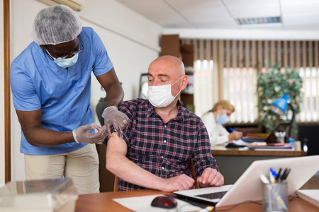 Medical worker vaccinates a man employee in a protective maskの写真素材