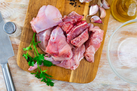 Raw sliced rabbit lying on wooden cutting board with seasonings