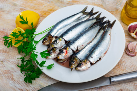 Sardines lying on white plate with lemon, parsley and garlicの写真素材