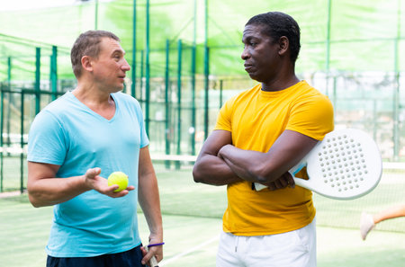 Men chatting on outdoor padel tennis courtの写真素材