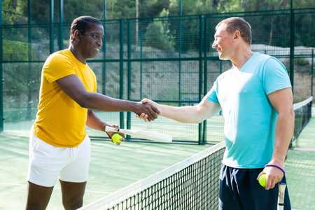 Two men padel tennis players shake hands amicablyの写真素材
