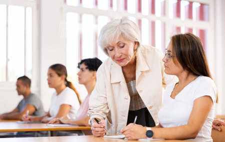 Elderly female teacher helping to solve problem to young girl studentの写真素材