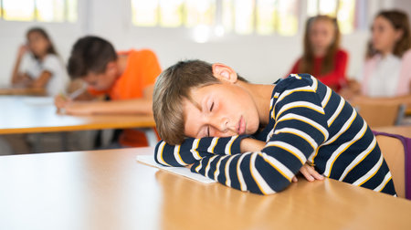Boy is tired and sleeping at the desk in classroomの写真素材