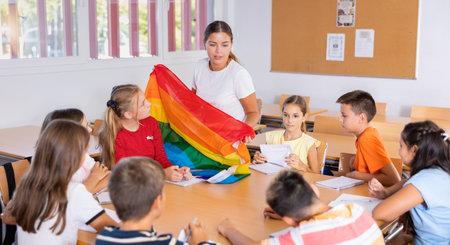 Children sitting in classroom and listening to female teacher. She holding rainbow flag in hands and talking about minoritiesの写真素材