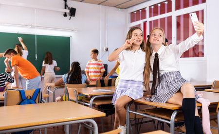 Cheerful girls classmates taking funny selfie with phone during breakの写真素材