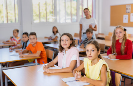 School kids with pens and notebooks studying in classroom with teacherの写真素材