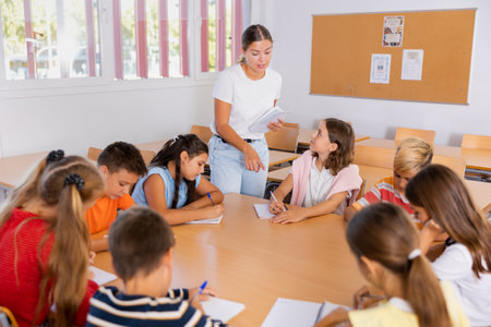 Friendly teacher explaining studying material to tweens sitting at common tableの写真素材