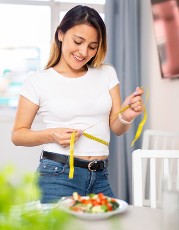 Colombian housewife measures waist before eating vegetable saladの写真素材