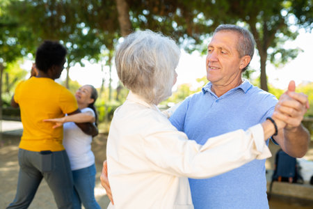 Cheerful multiracial middle aged and older adults enjoying dancing in pairs outdoor at parkの写真素材