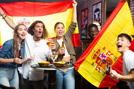 Happy international sport supporters holding up the flag of Spain and drinking beer in the pubの写真素材