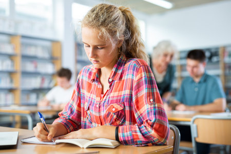 Teenager girl with a laptop studying in school libraryの写真素材