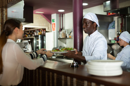African american chef serving ready tasty meals to visitors of restaurantの写真素材
